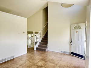 Entry foyer featuring neutral-toned tile flooring, a white paneled entry door with an arched transom, and a carpeted staircase with white railings