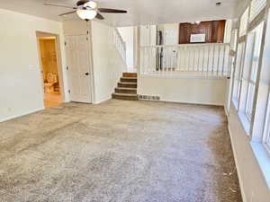 Carpeted living area featuring a ceiling fan with integrated lighting, multiple windows with louvered shutters, and a staircase with a white baluster railing