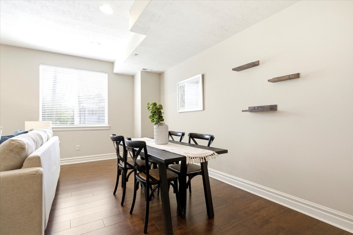 Open-concept living area featuring rich wood-finish flooring, recessed lighting, and a large window with blinds