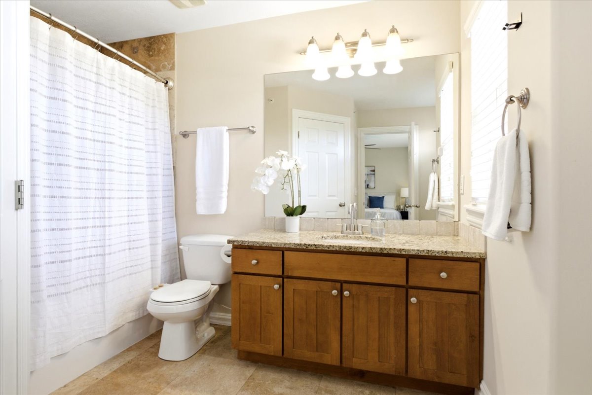 Full bathroom featuring a wood-finish vanity with a light-toned countertop, a large wall mirror, and a five-light fixture