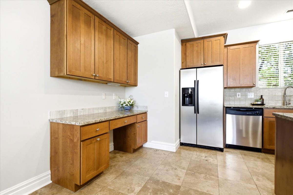 Kitchen featuring wood-finish cabinetry, granite countertops, tile flooring, stainless steel appliances, and a built-in desk area