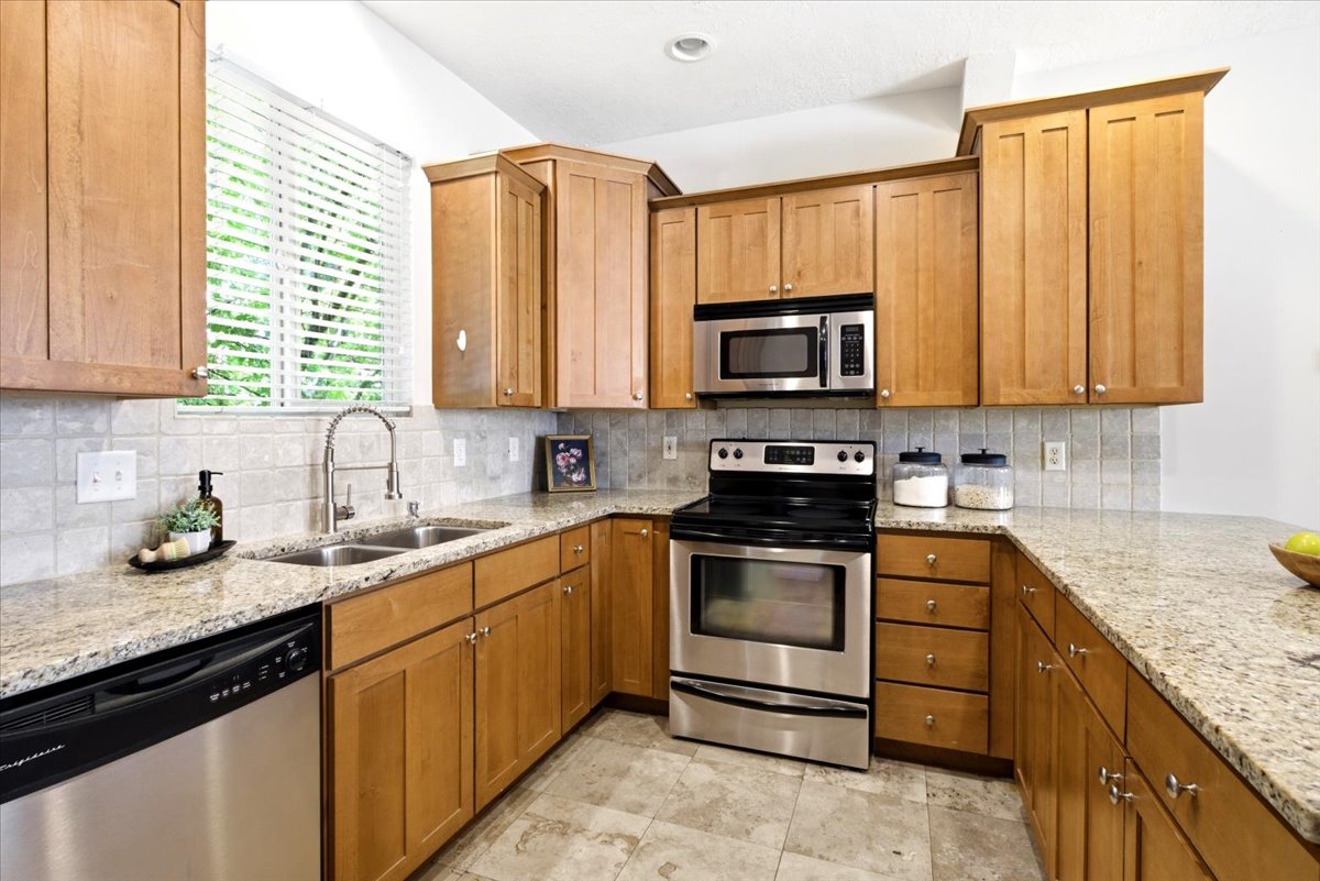 Kitchen featuring wood cabinetry, stainless steel appliances, granite countertops, a double basin sink, and a tile backsplash