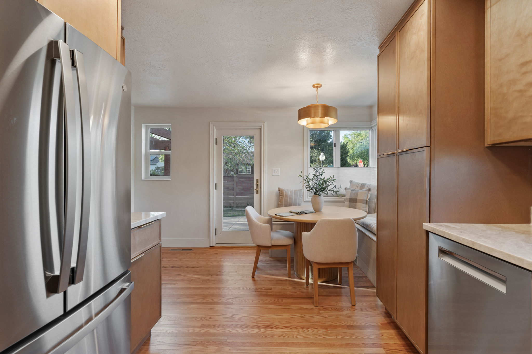Kitchen with wood-finish flooring, stainless steel appliances, light wood cabinetry, and a built-in dining nook with bench seating