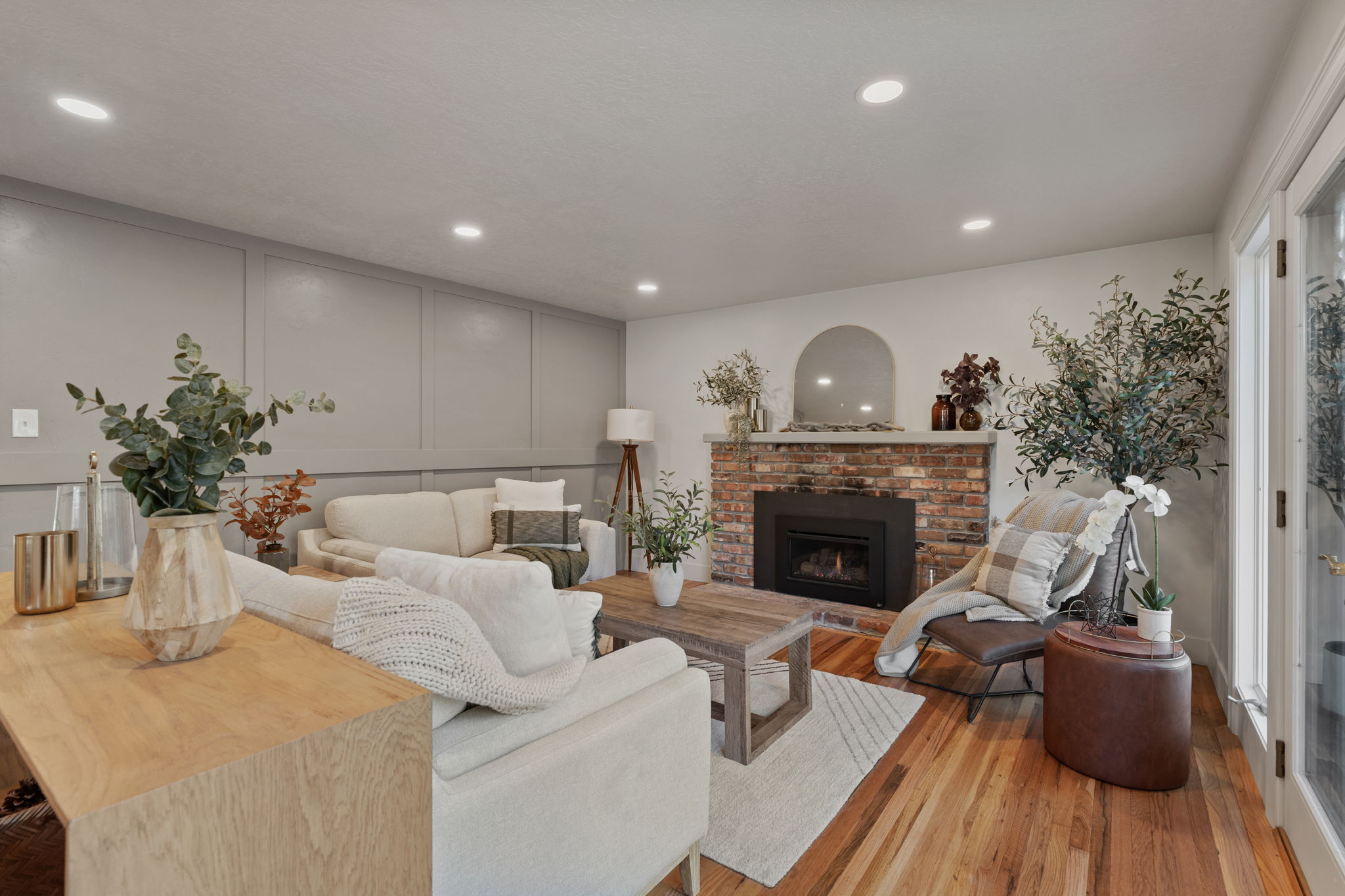 Living space featuring a brick fireplace with a black insert, wood-finish flooring, recessed lighting, wall paneling, and an arched mirror above the mantel