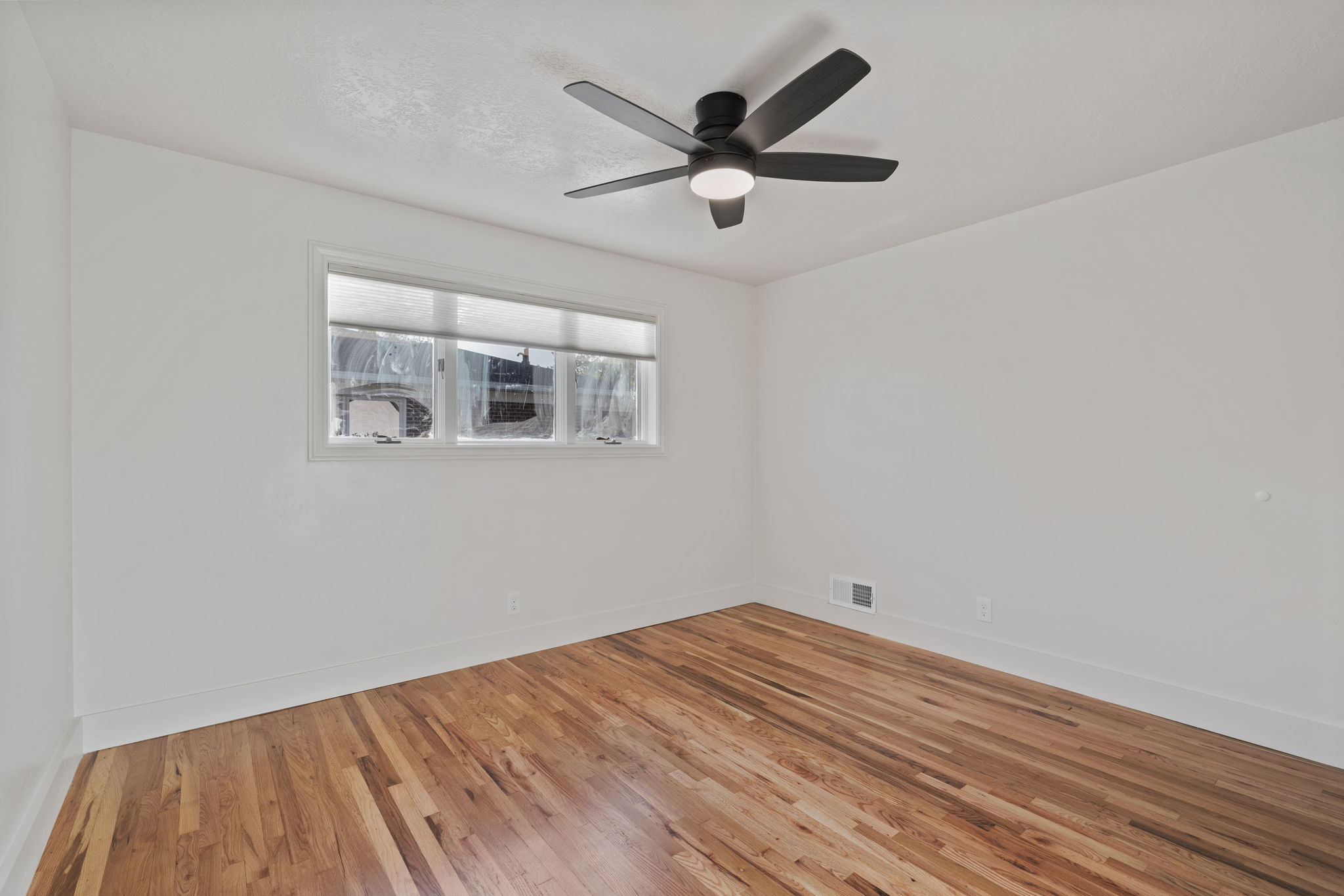 Room featuring wood-finish flooring, white walls, and a multi-pane window with blinds