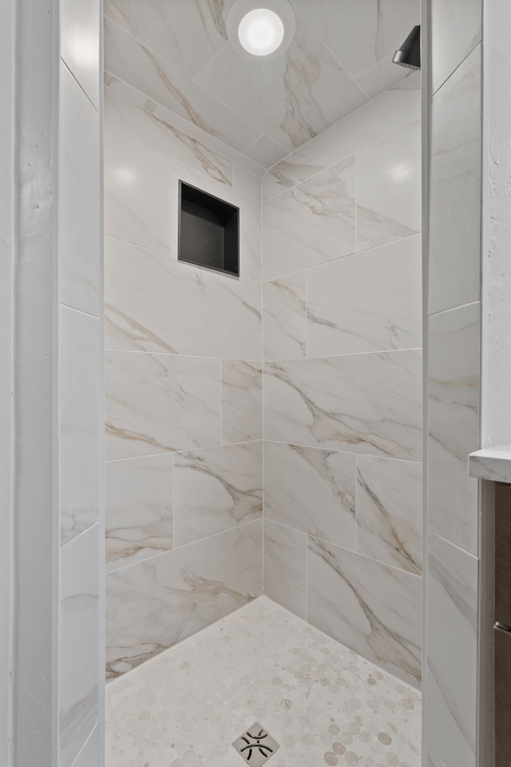 Shower with marble-look wall tiles, recessed niche, circular ceiling light, and mosaic-tiled floor