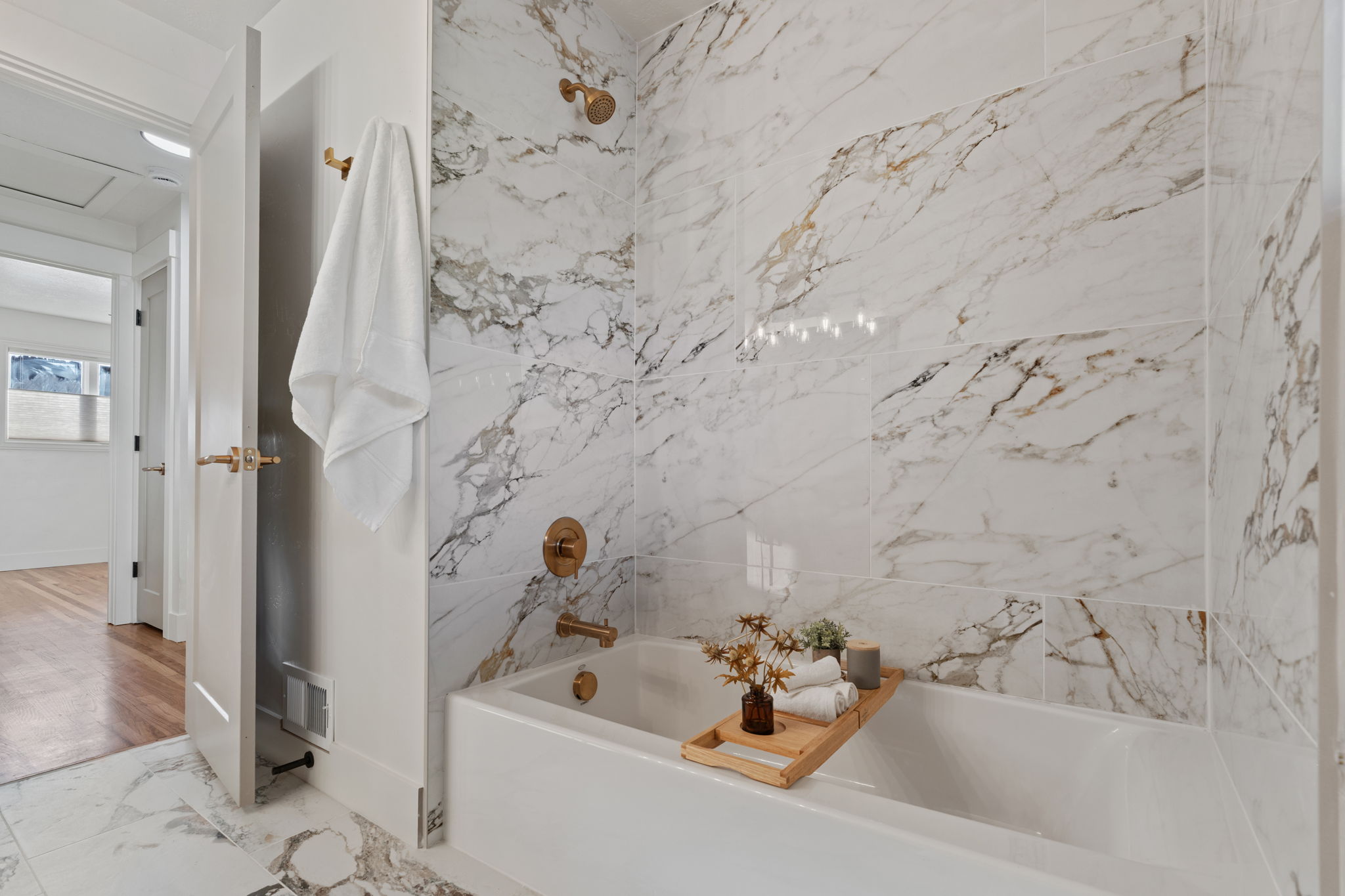 White soaking tub with gold-finish fixtures and full-height marble-style tile surround