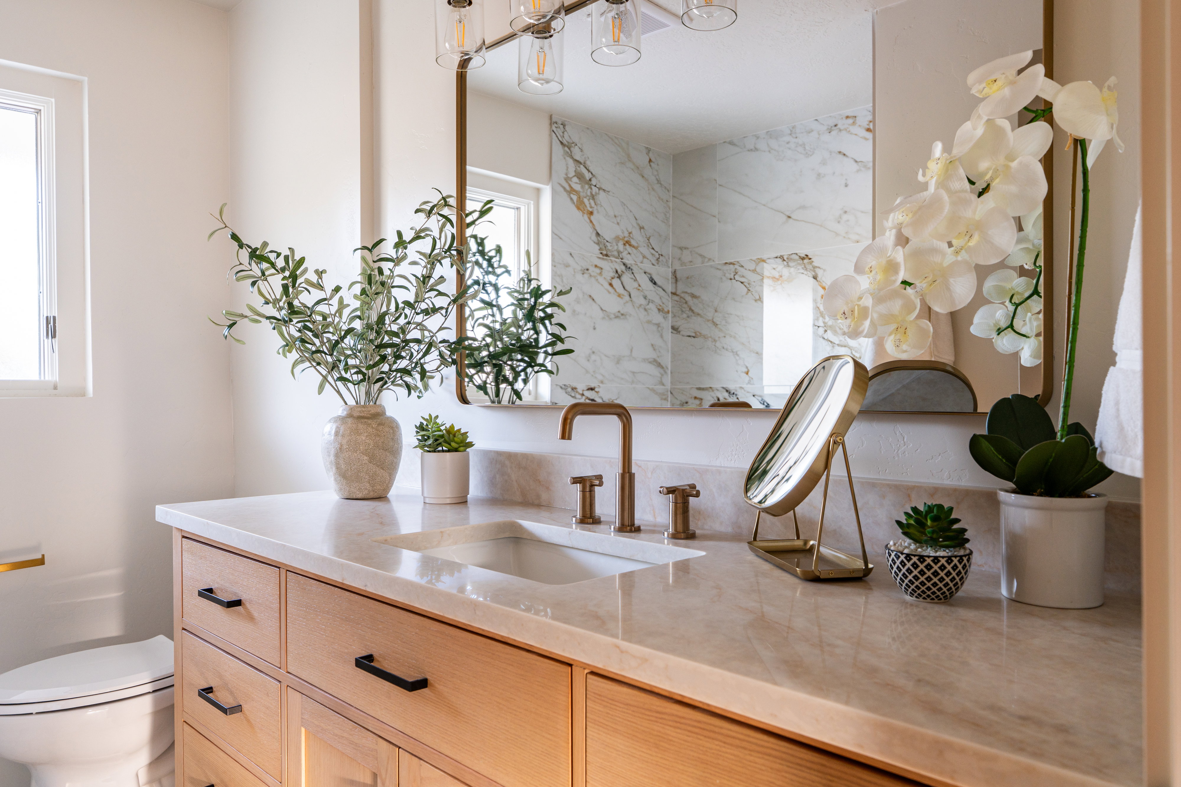Bathroom vanity featuring a light wood-finish cabinet with matte black hardware, integrated sink, and stone countertop