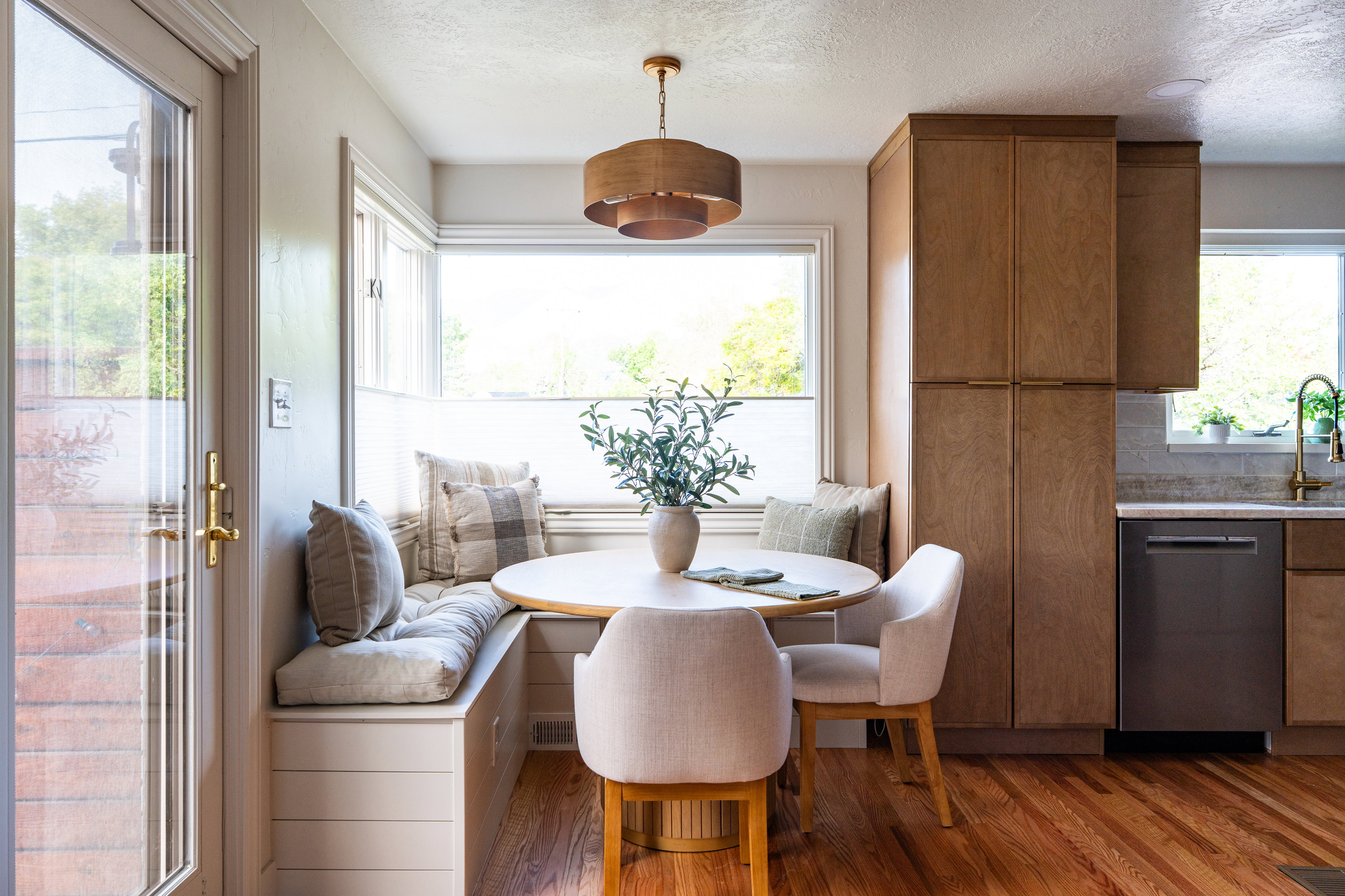 Integrated breakfast nook with built-in bench seating, large bay windows, wood-finish flooring, full-height cabinetry, and a modern drum pendant light fixture
