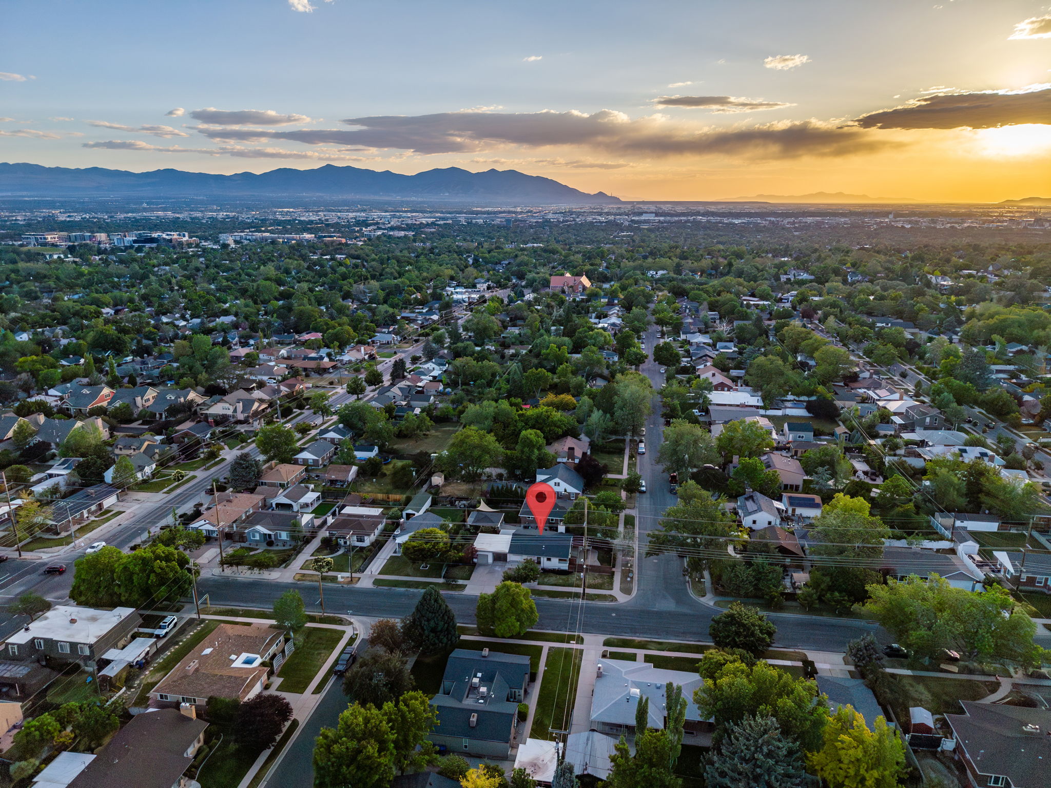 Residential streetscape featuring mature tree cover, paved roadways, and a distant mountain range backdrop under an expansive sky