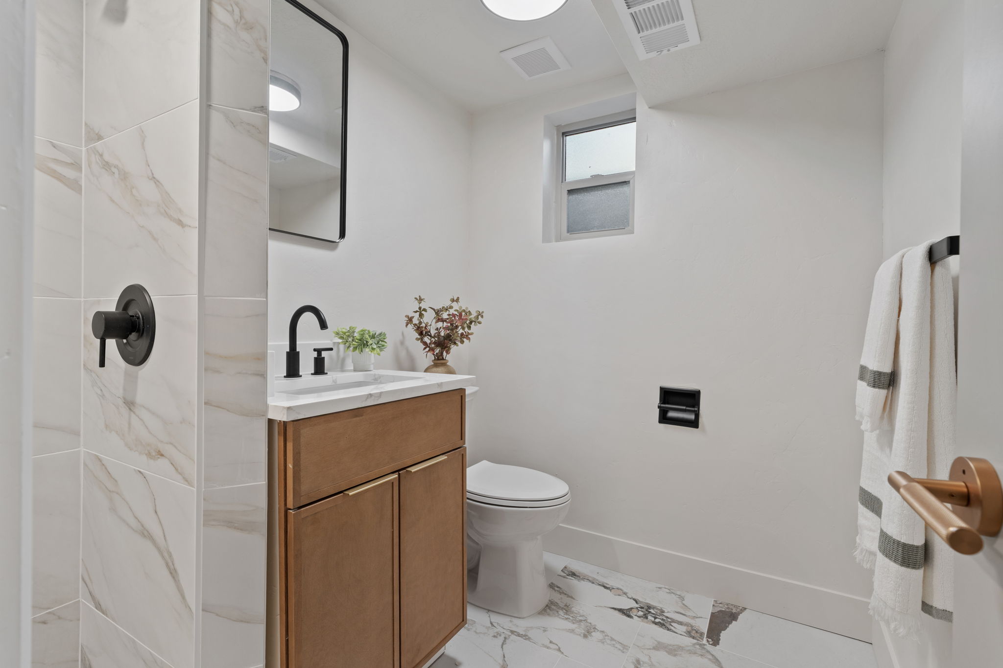 Bathroom featuring a wood-finish vanity with a white countertop, matte black faucet, and rectangular mirror