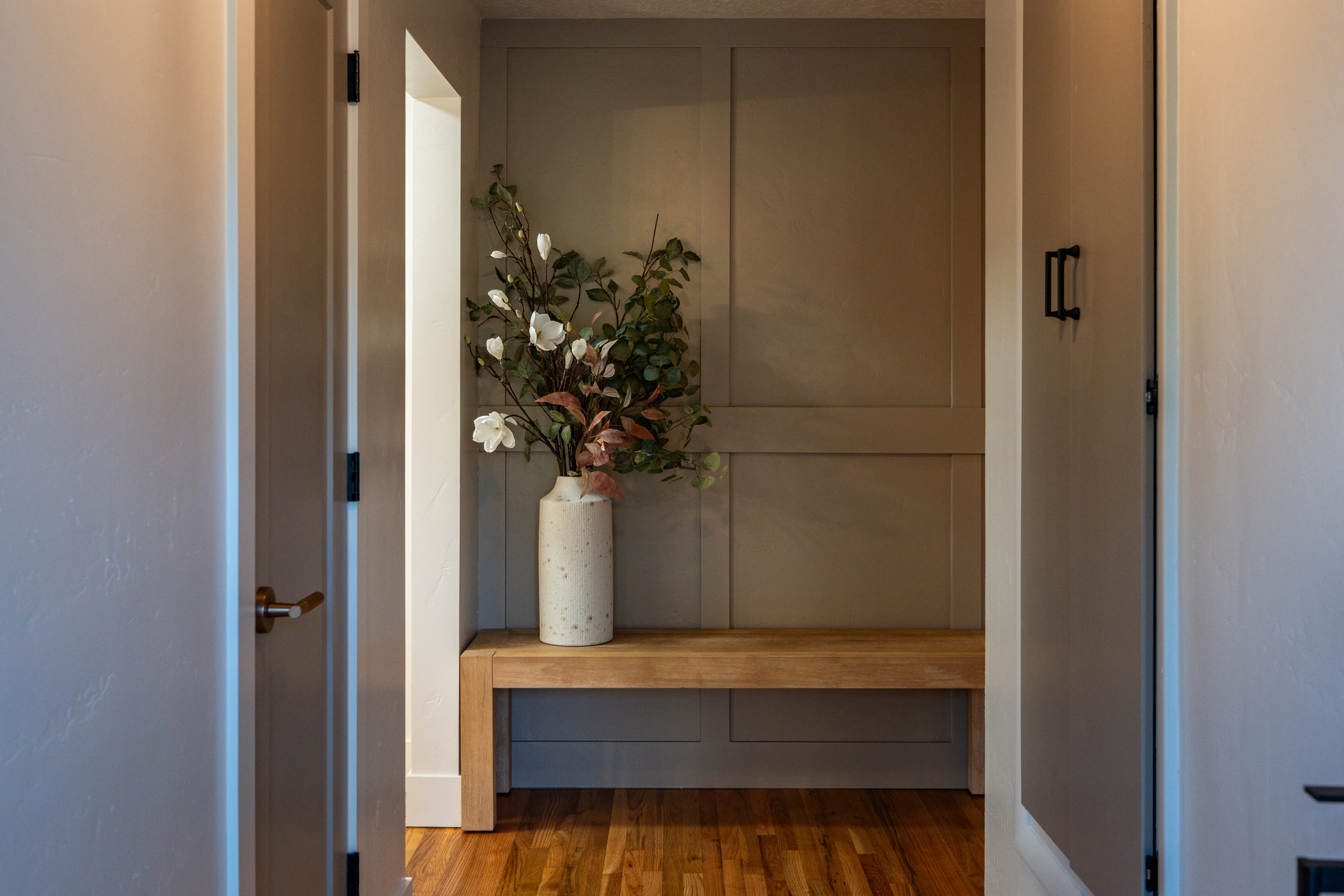 Paneling accent wall with an integrated wooden bench, complemented by natural wood-finish flooring