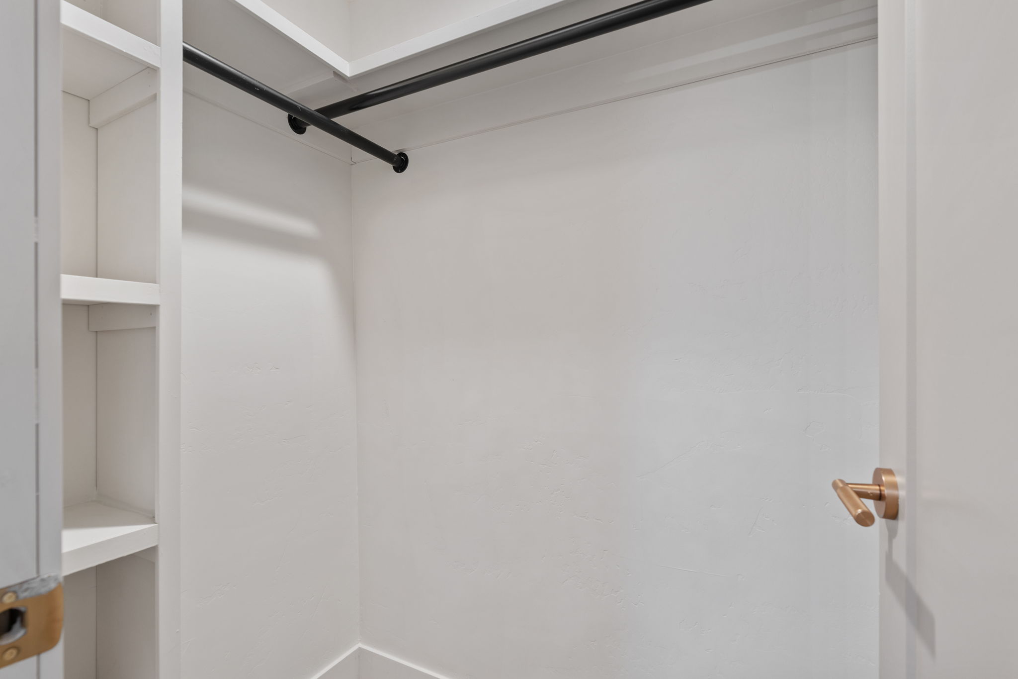 White closet interior featuring built-in shelving, a black hanging rod, and a gold-toned door handle