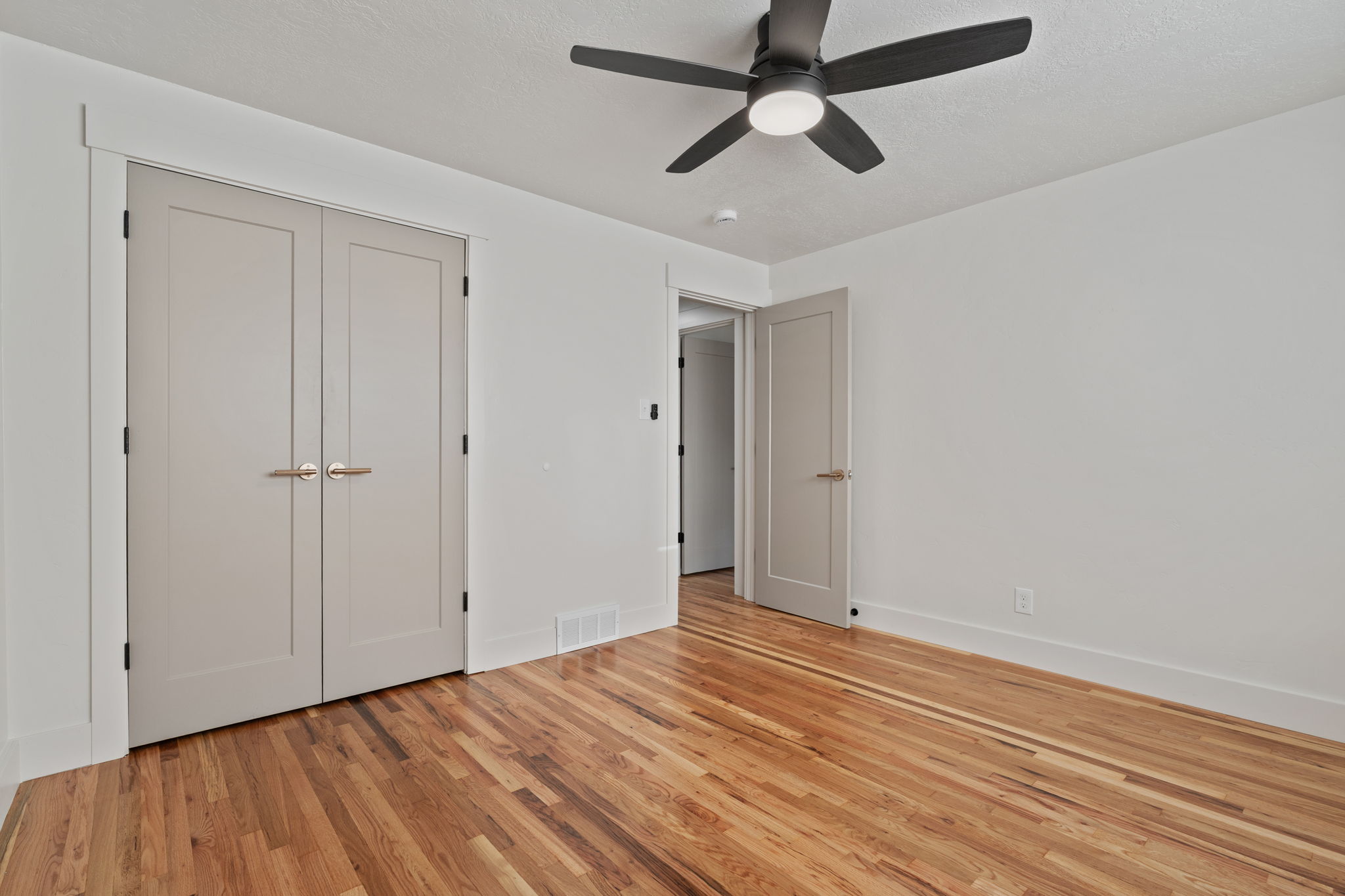 Spacious room featuring hardwood flooring, a contemporary ceiling fan, and white painted walls