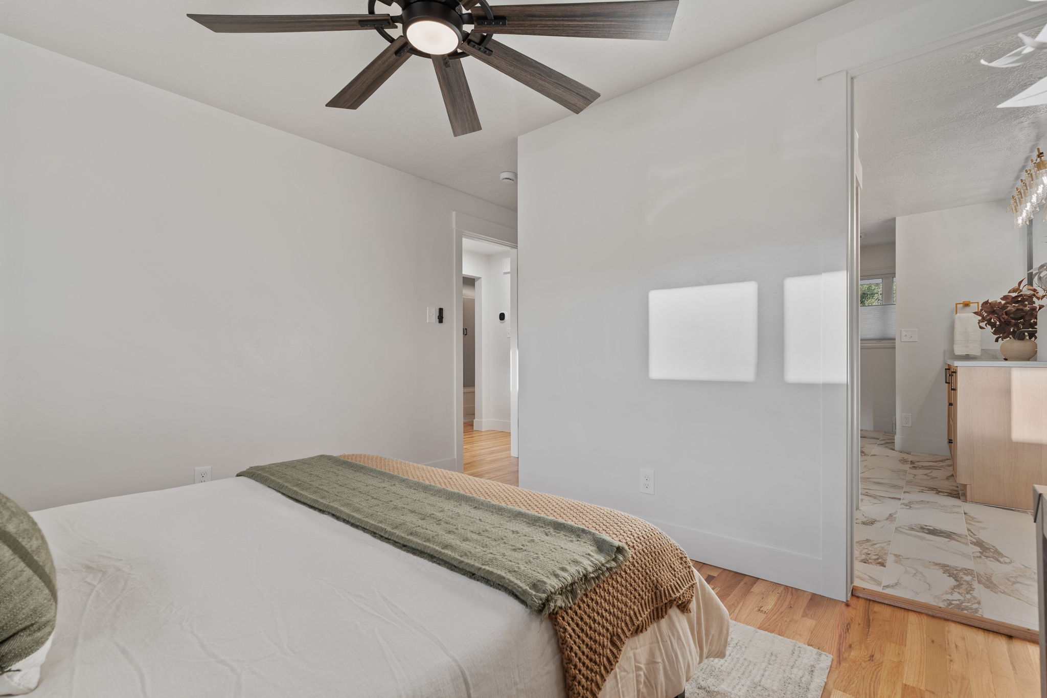 Hardwood-finish flooring extending into the hallway, a ceiling fan with integrated lighting, and white walls