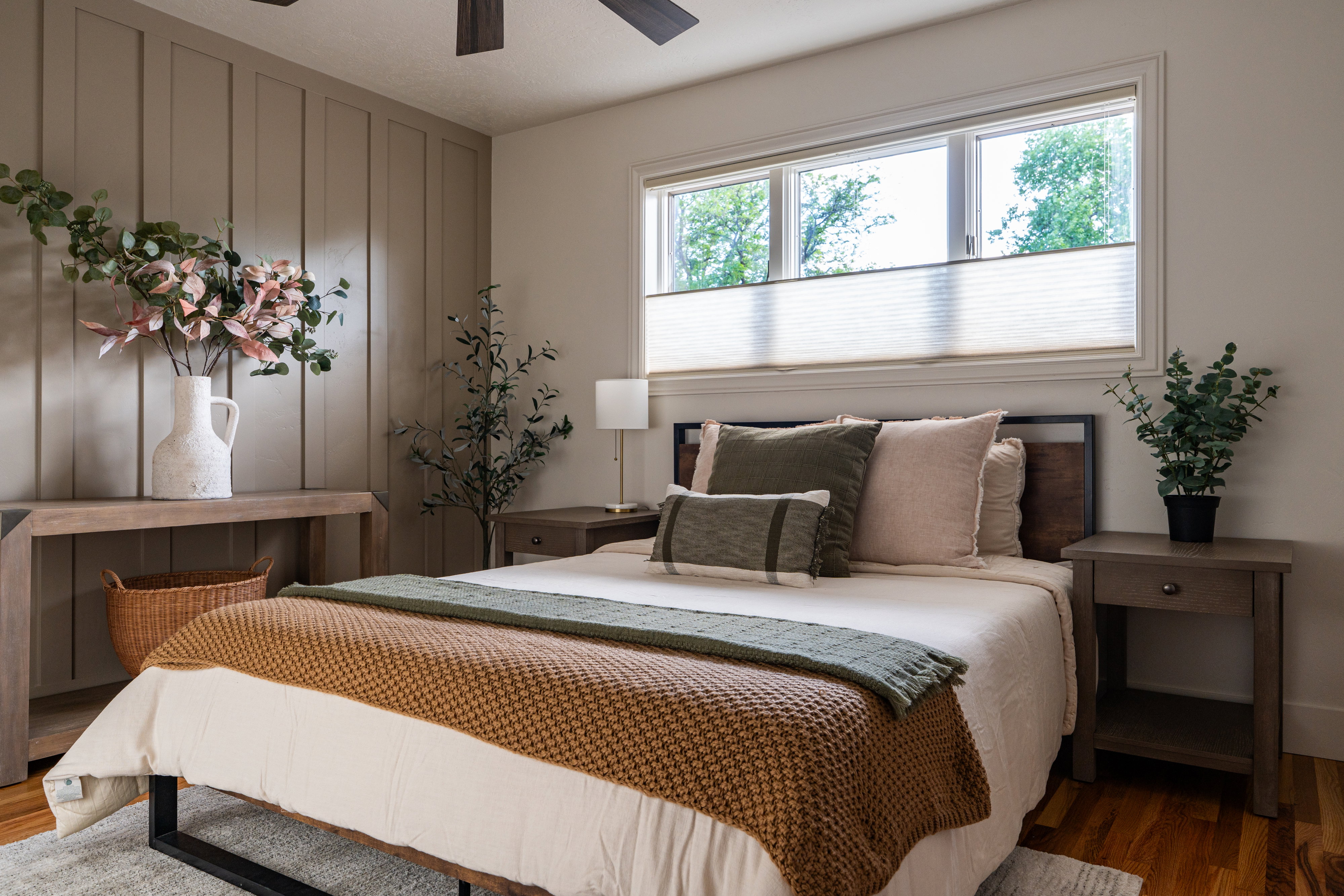 Bedroom featuring a board and batten accent wall, wood-finish flooring, a contemporary ceiling fan, and a wide window with privacy blinds