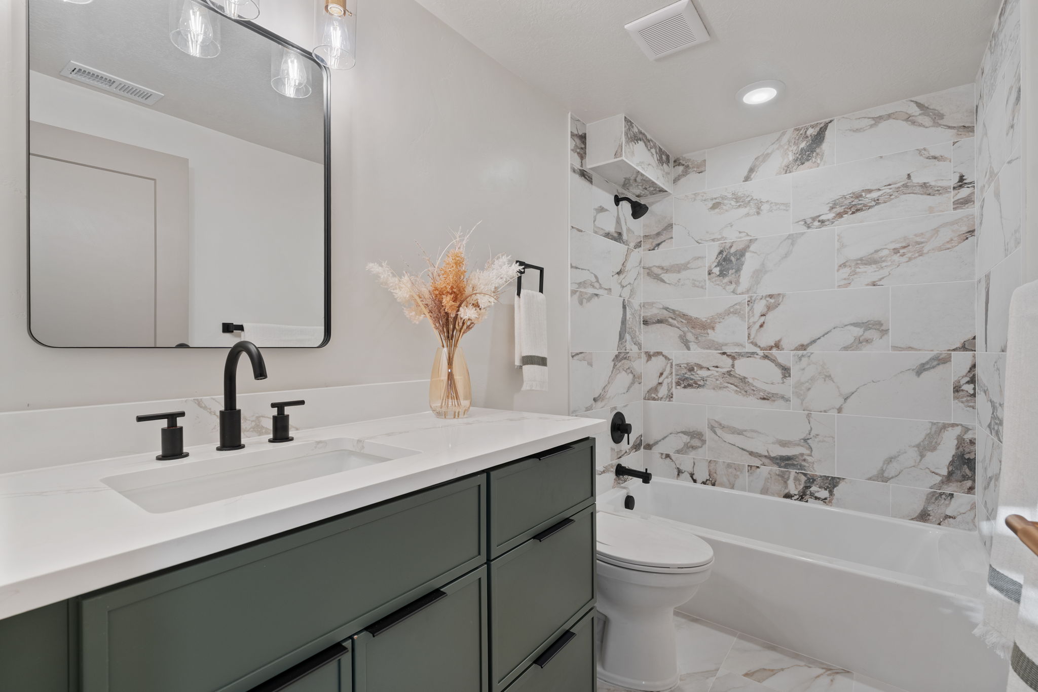 Bathroom featuring a vanity with dark green cabinetry, white countertop with integrated sink, and matte black fixtures