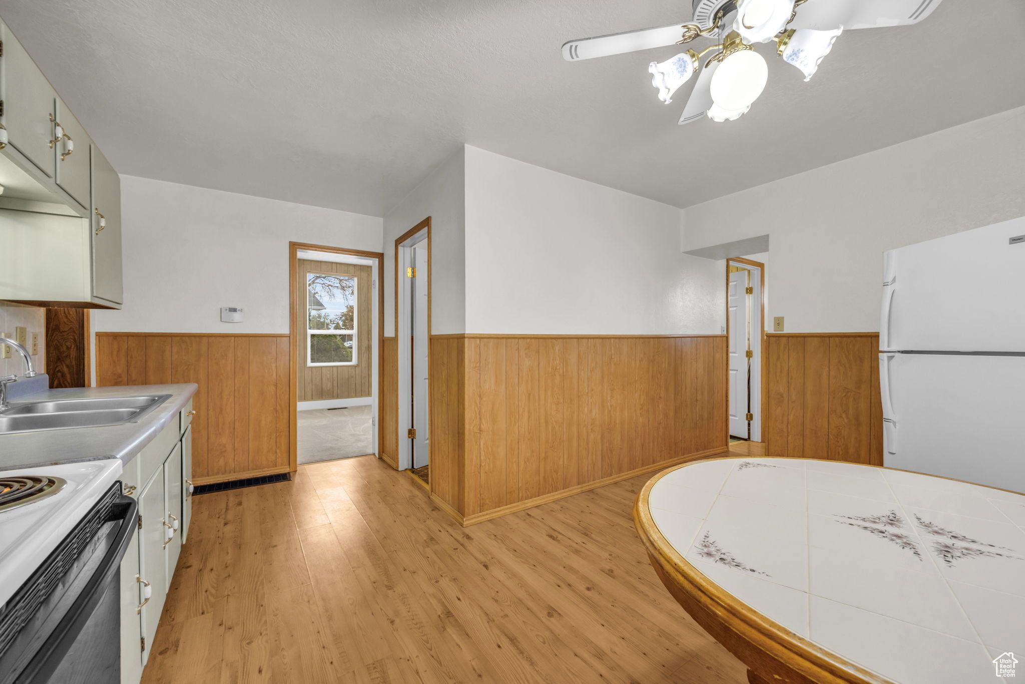 Kitchen space featuring wood-finish flooring, white walls with wood wainscoting, and a white ceiling fan with light fixture