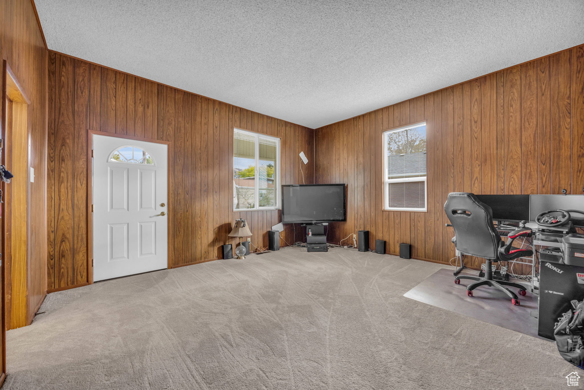 Spacious room featuring wood-finish paneling, light-colored carpeting, and a white paneled entry door with an arched decorative glass insert