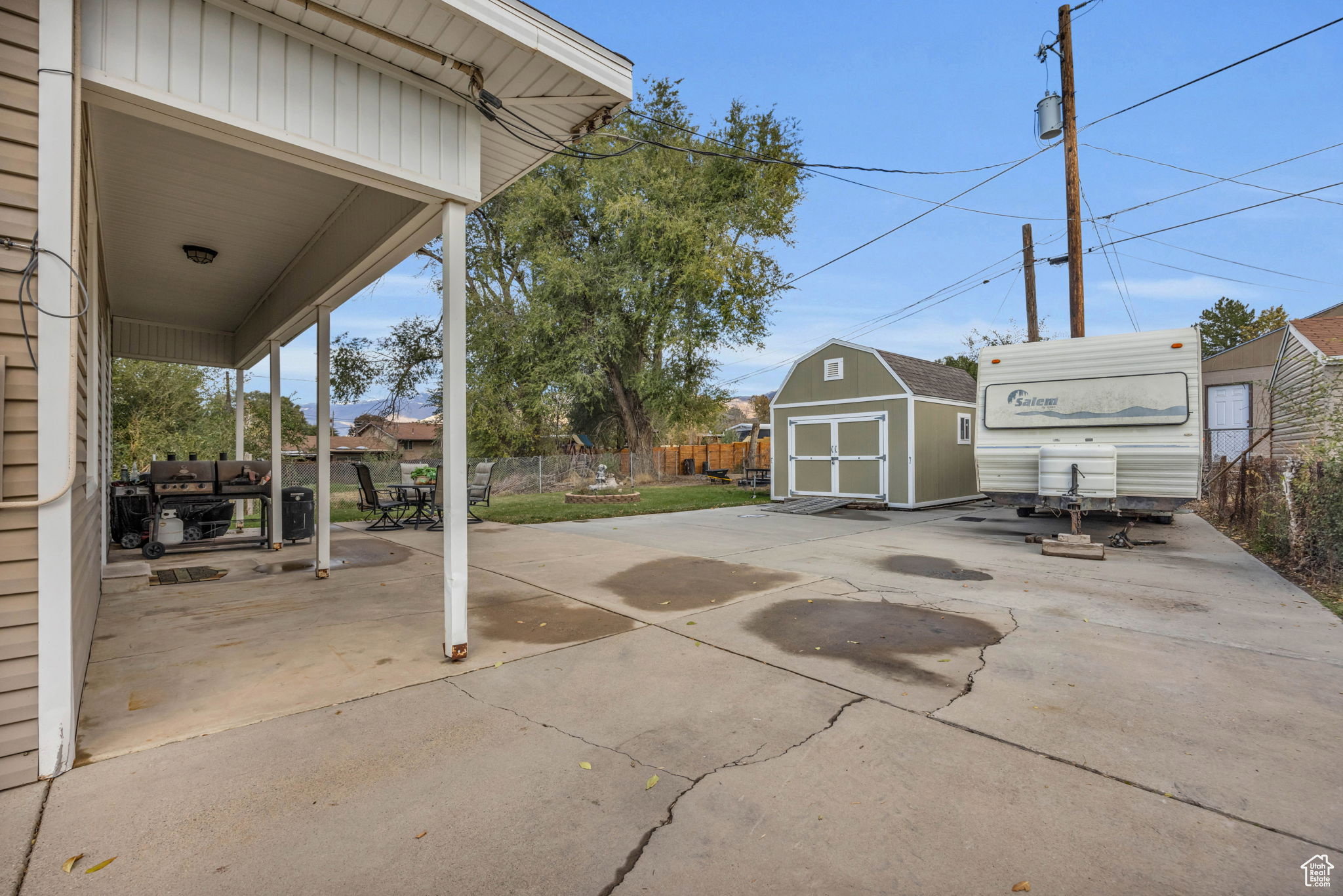 Covered concrete patio with white support columns, concrete driveway, and detached storage shed