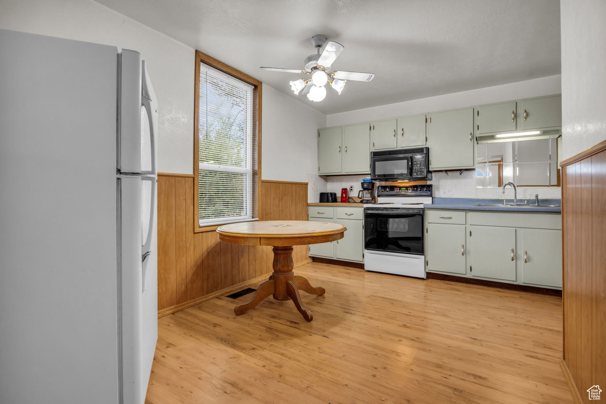 Kitchen featuring light wood-finish flooring, light green cabinetry, a built-in microwave, and a ceiling fan with light fixture