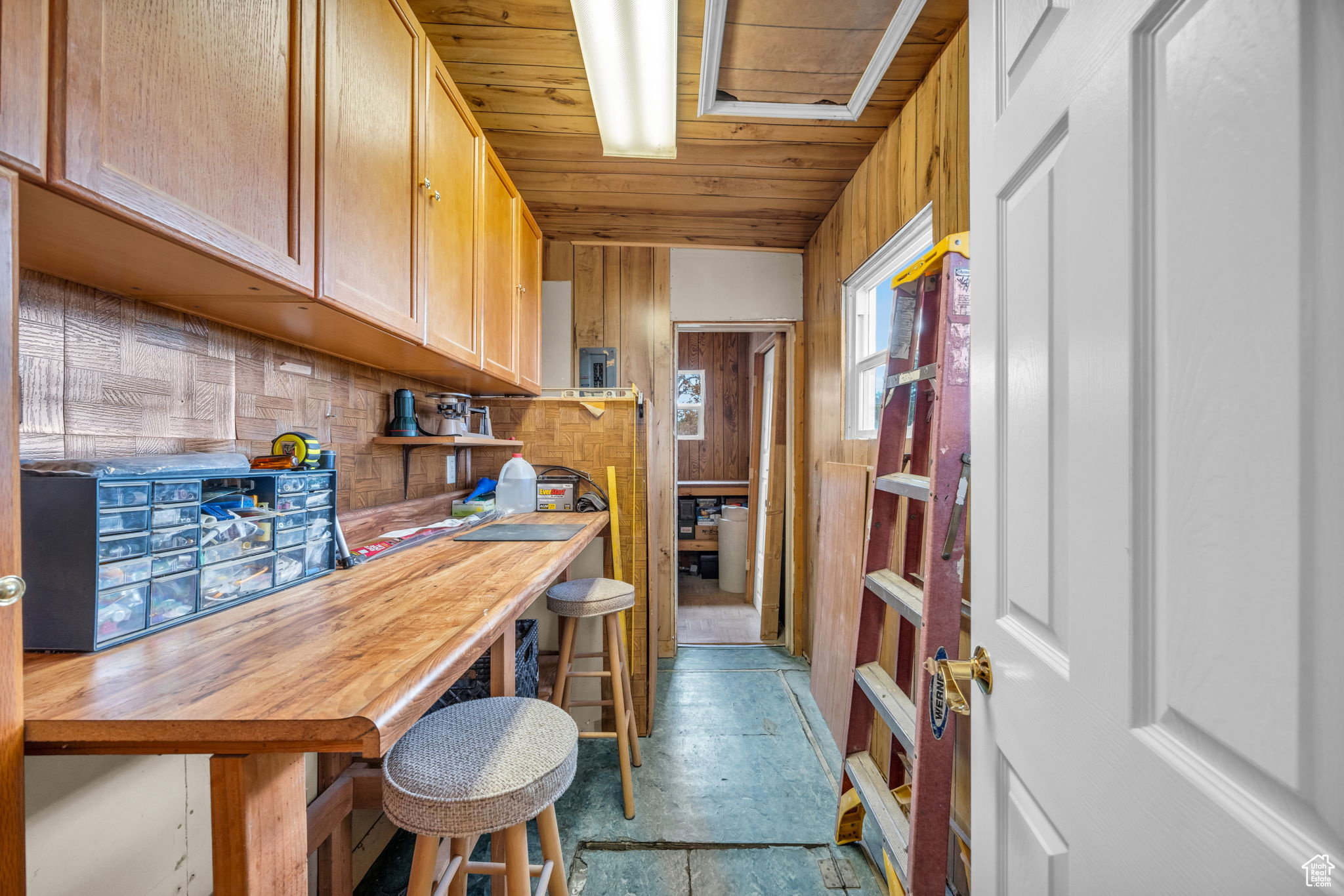Workroom featuring a long wood-finish countertop, extensive overhead cabinetry, and wood-paneled walls