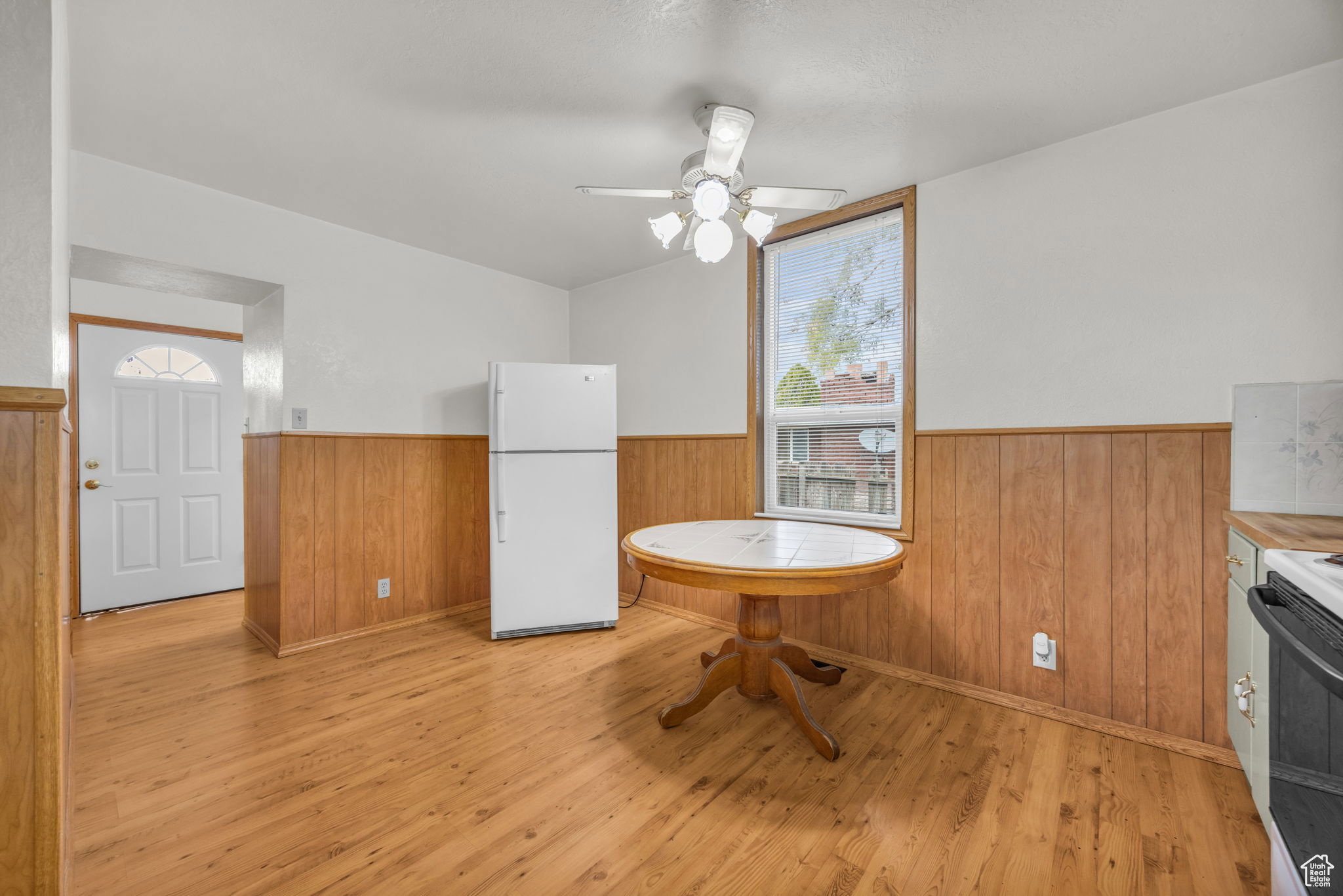 Well-lit eat-in kitchen area featuring wood-finish flooring, wood paneling, and a ceiling fan with integrated lighting