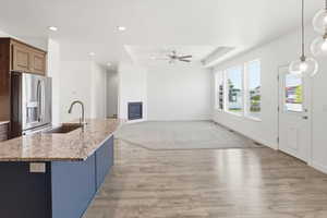 Open-concept living space with wood-finish flooring, a kitchen island featuring a granite countertop and undermount sink, and a stainless steel refrigerator