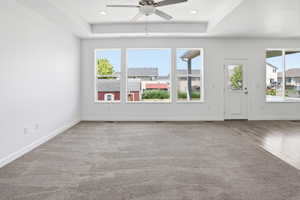 Spacious room featuring a tray ceiling with a ceiling fan, recessed lighting, and a combination of carpet and wood-finish flooring
