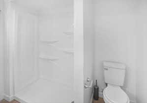 White acrylic shower enclosure with integrated shelving and a white toilet with chrome flush buttons