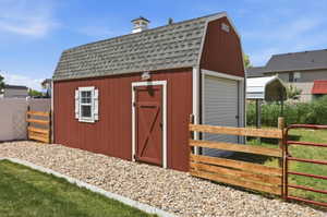 Red barn-style shed featuring a gray shingle roof, cupola, white window with shutters, and a roll-up garage door