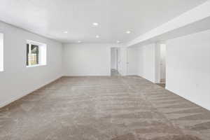 Spacious lower-level room featuring light gray carpeting, recessed lighting, white walls, and two white-framed windows