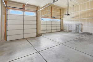 Spacious two-car garage featuring segmented white doors with upper window panels, concrete flooring, and an exposed concrete foundation wall