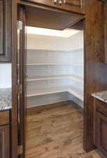 Spacious walk-in pantry with wood-finish flooring, ample white shelving, and recessed lighting
