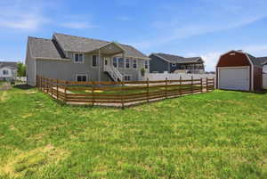 Expansive backyard featuring a red barn-style shed with a garage door, a wooden split-rail fence, and a covered patio with white railings and stairs