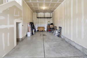 Spacious garage with unfinished drywall, concrete flooring, and an overhead storage rack