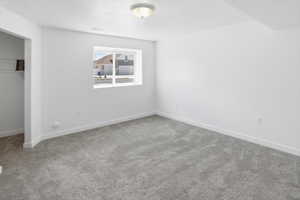 Spacious room featuring light gray carpeting, crisp white walls, a single window, and a built-in closet with wire shelving