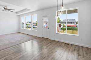 Spacious open-concept room featuring light wood-finish flooring, a tray ceiling with a ceiling fan, and large windows