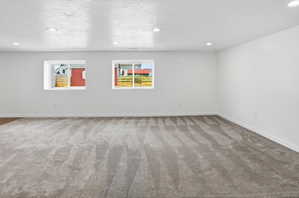 Spacious room featuring gray carpeting, recessed lighting, white walls, and two egress windows providing natural light