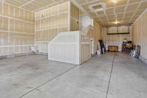 Two-car deep garage with concrete flooring, unfinished drywall, and a built-in staircase