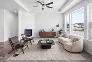 Spacious living area featuring a corner-mounted fireplace, multiple large windows, tray ceilings, recessed lighting, and a ceiling fan