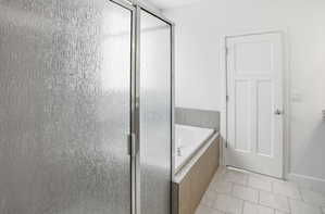 Frosted glass shower enclosure featuring a corner soaking tub with tiled surround, white three-panel interior door, and light-toned tile flooring