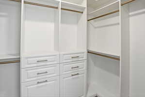 Custom closet organization system featuring white cabinetry, multiple shelving units, integrated drawers with brushed nickel hardware, and brass hanging rods