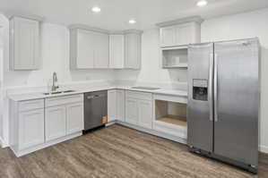 Modern kitchen featuring white shaker cabinetry, light-toned countertops, stainless steel appliances, and wood-finish flooring