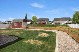 Spacious backyard featuring a red barn-style shed with a gambrel roof, a gravel pathway, a light wood three-rail fence, and a white privacy fence