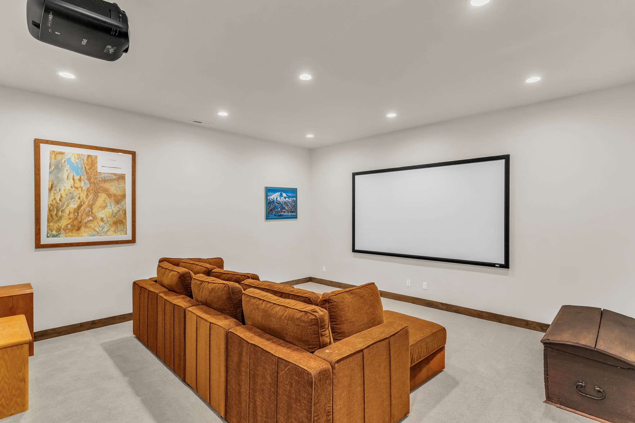 Dedicated media room featuring a ceiling-mounted projector, large wall-mounted screen, recessed lighting, and light-toned carpeting