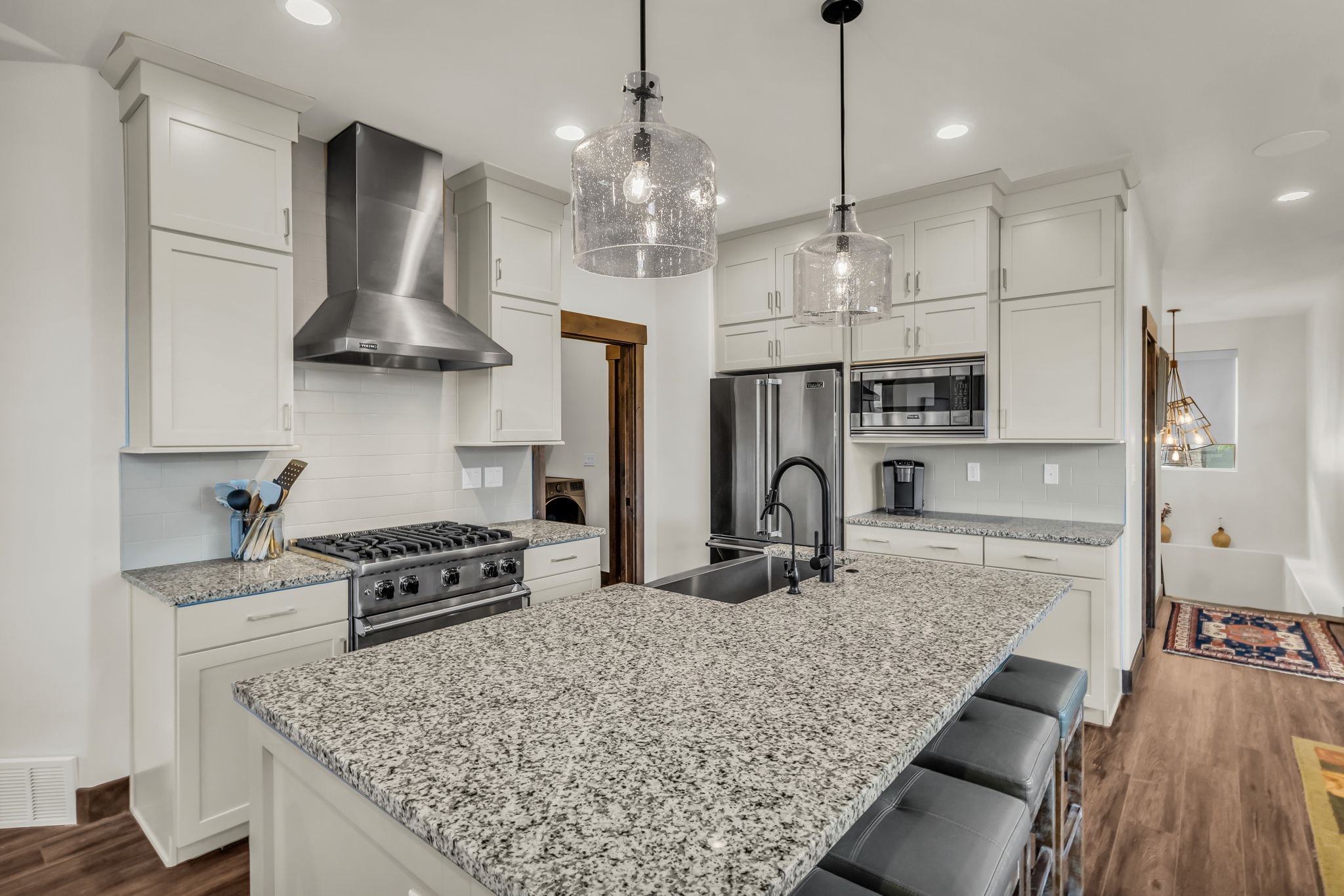 Bright kitchen featuring a central island with granite countertops, white cabinetry, stainless steel appliances, and wood-finish flooring