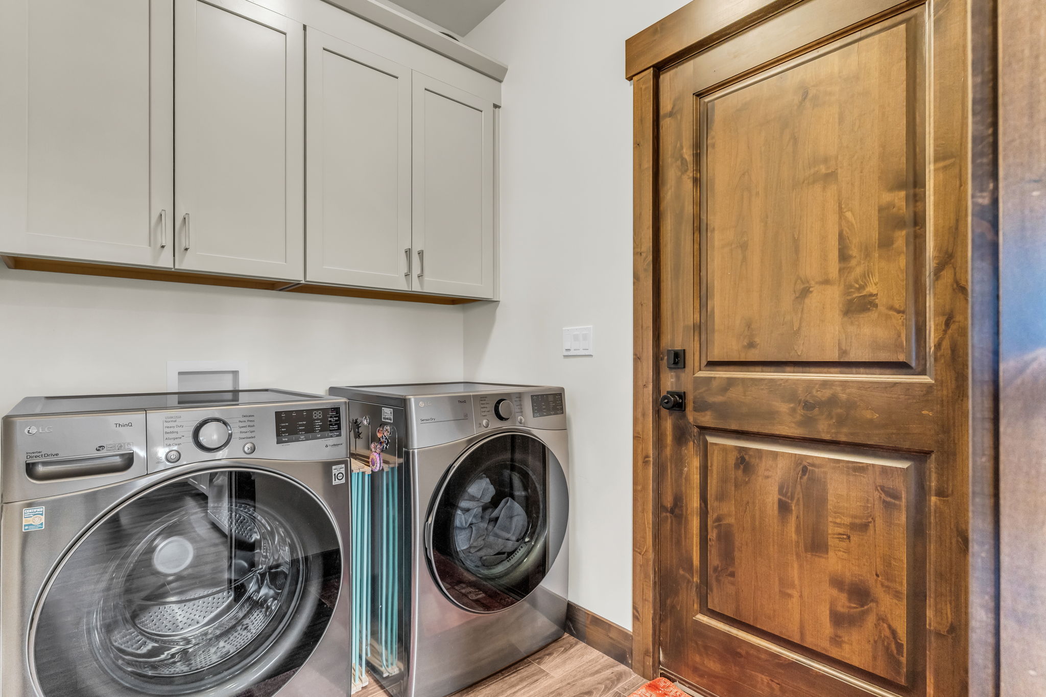 Utility area featuring light-toned upper cabinetry, wood-finish flooring, and a paneled wooden door with a matte black handle