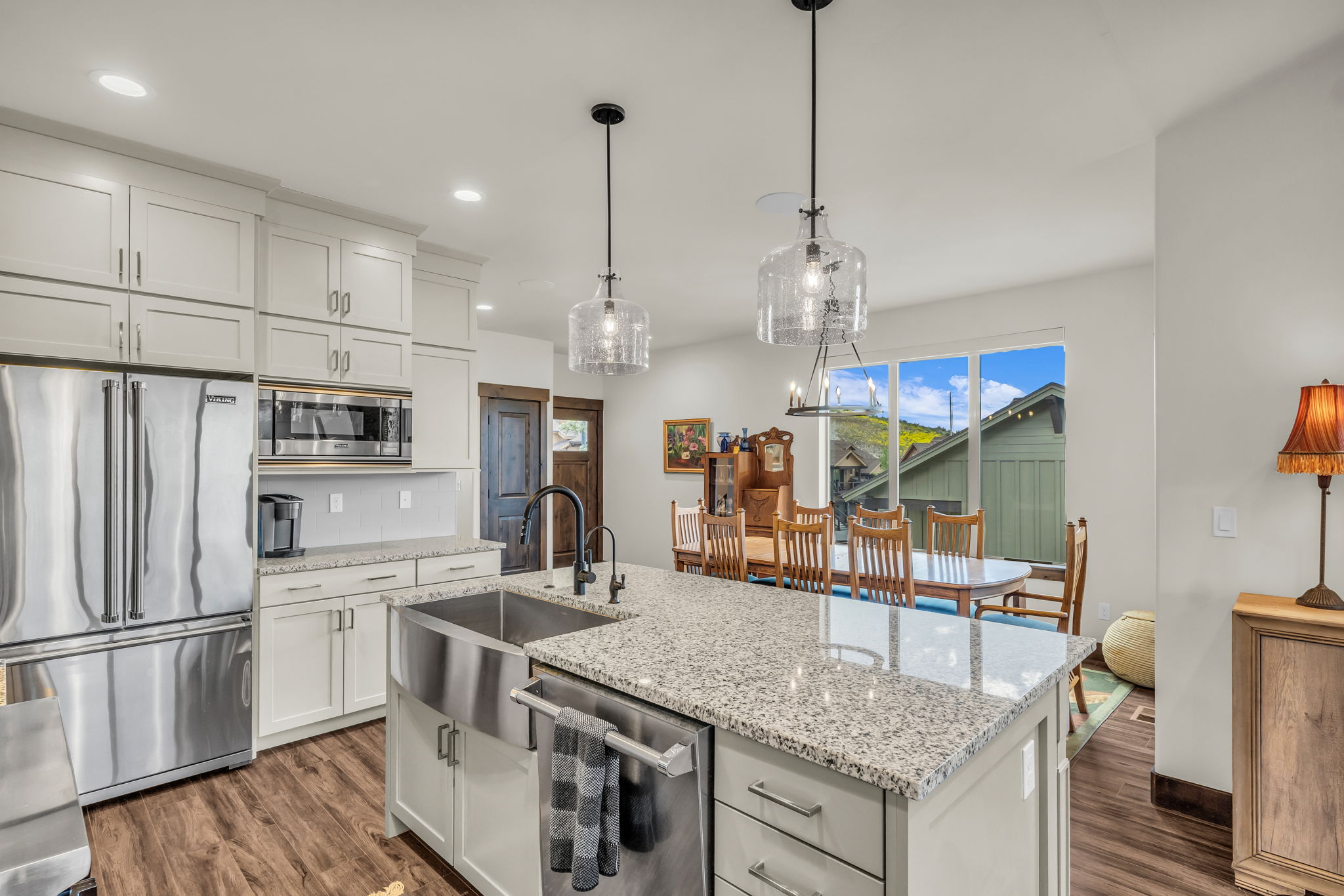 Modern kitchen featuring light-toned cabinetry, stainless steel appliances, wood-finish flooring, granite countertops, and a large farmhouse sink