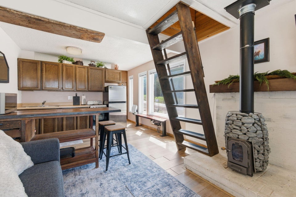 Living area featuring a stone-clad wood-burning stove with a black flue, a wooden ladder, and wood-finish flooring
